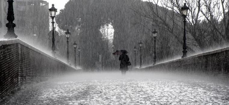 A man walks across a bridge with an umbrella in the rain